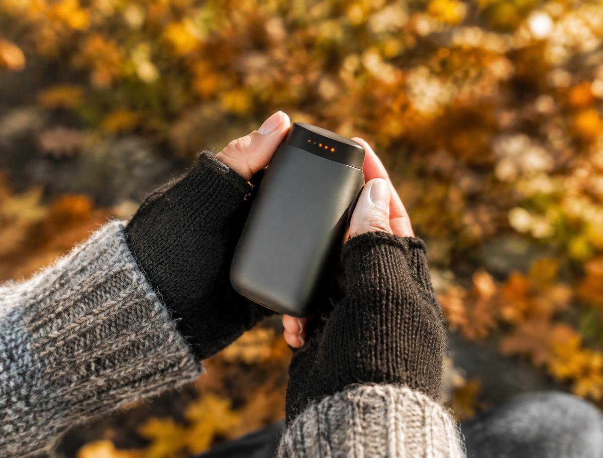Hands holding a compact hand warmer outdoors